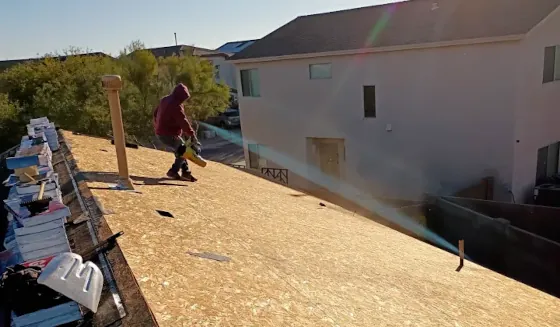 A roof repair project showing a worker using a blower to remove debris from the surface of a roof undergoing repairs.